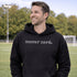Person wearing “Soccer Nerd” hoodie holding a soccer ball on a soccer field during a game, casual athletic soccer apparel