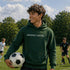 Person wearing “Soccer Nerd” hoodie holding a soccer ball on a soccer field during a game, casual athletic soccer apparel