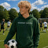 Person wearing “Soccer Nerd” hoodie holding a soccer ball on a soccer field during a game, casual athletic soccer apparel
