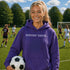 Person wearing “Soccer Nerd” hoodie holding a soccer ball on a soccer field during a game, casual athletic soccer apparel