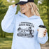 woman wearing grey hoodie with “Somebody’s Loud Mouth Soccer Mama” design featuring mom yelling on soccer sideline with kids playing in background