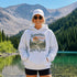 Vintage mountain adventure hoodie featuring a scenic outdoor landscape graphic on a Gildan 18500 Heavy Blend hoodie, shown in a lifestyle mockup. Available in multiple colors with a relaxed unisex fit.