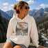 Vintage mountain adventure hoodie featuring a scenic outdoor landscape graphic on a Gildan 18500 Heavy Blend hoodie, shown in a lifestyle mockup. Available in multiple colors with a relaxed unisex fit.