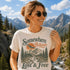 Woman wearing a t-shirt with nature-themed design and mountains in the background