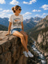 Person sitting on a rock with a scenic mountain view, wearing a t-shirt with text and graphics.