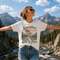 Woman wearing a t-shirt with 'Somewhere Between Lost & Free' design in a mountainous landscape.