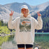 Vintage mountain adventure hoodie featuring a scenic outdoor landscape graphic on a Gildan 18500 Heavy Blend hoodie, shown in a lifestyle mockup. Available in multiple colors with a relaxed unisex fit.