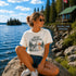 Woman sitting by a lake wearing a 'Still Waters' t-shirt with nature-themed design.