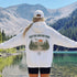 Vintage-inspired outdoor hoodie featuring a matching left chest graphic and large back graphic, displayed in a lifestyle mockup inspired by hiking, camping, scenic mountain roads, and outdoor adventures.