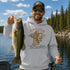 A man wearing a cream-colored hoodie with a graphic of Bigfoot fishing and the text 'TIGHT LINES No Deadlines' stands by a lake with trees in the background.