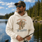 A man wearing a cream-colored hoodie with a graphic of Bigfoot fishing and the text 'TIGHT LINES No Deadlines' stands by a lake with trees in the background.