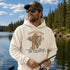 A man wearing a cream-colored hoodie with a graphic of Bigfoot fishing and the text 'TIGHT LINES No Deadlines' stands by a lake with trees in the background.