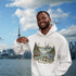Man wearing a hoodie with Ontario-themed design in front of a city skyline and water body.
