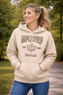 Woman wearing beige Maple Syrup Fan Club hoodie with maple leaf graphic, smiling outdoors in a natural setting with trees in the background