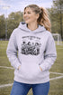 Soccer mom hoodie with “Sideline Social Club” design featuring moms sitting in lawn chairs drinking coffee while watching kids play soccer in the background