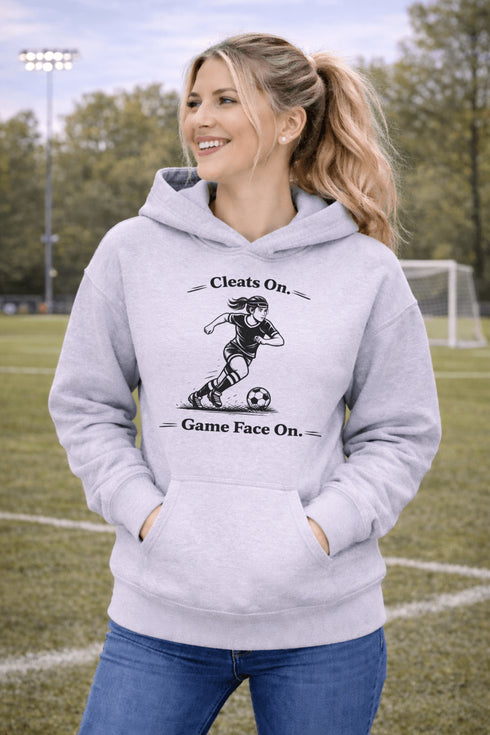 Woman wearing a Cleats On Game Face On soccer hoodie with player graphic, holding coffee outdoors