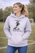 Woman wearing a Cleats On Game Face On soccer hoodie with player graphic, holding coffee outdoors