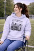 Soccer mom hoodie with “Sideline Social Club” design featuring moms sitting in lawn chairs drinking coffee while watching kids play soccer in the background