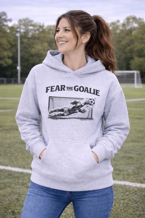 woman wearing grey hoodie with “Fear The Goalie” soccer goalkeeper design featuring diving goalie making a save
