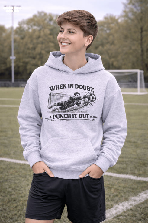 Teenaged boy wearing grey hoodie with “When In Doubt Punch It Out” soccer goalie design featuring diving goalkeeper making a save