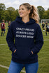 Woman wearing a navy hoodie with 'Crazy proud always loud soccer mom' text on a soccer field.
