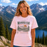Woman wearing Wander Far Take the Scenic Route mountain hiking graphic t-shirt featuring vintage mountain landscape artwork with pine trees and sunset background.