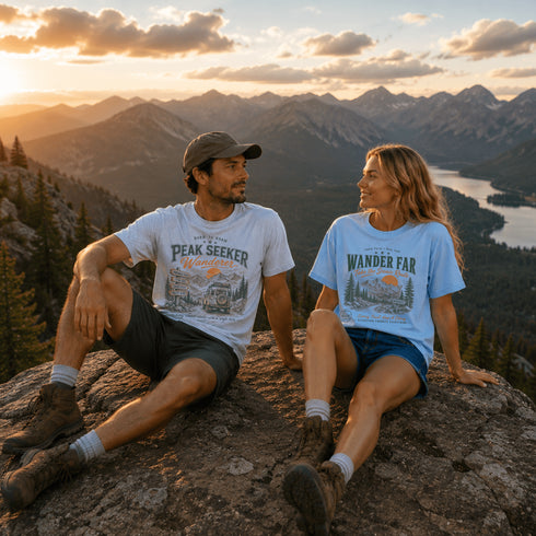 Two people sitting on a mountain top with scenic view and 'Peak Seeker' t-shirts.