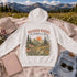 Vintage mountain and wildflower graphic hoodie featuring a matching left chest design and oversized back print on a unisex Gildan 18500 Heavy Blend hoodie available in multiple colors. Perfect for hiking, camping, outdoor adventures, and everyday wear.