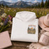 Vintage mountain and wildflower graphic hoodie featuring a matching left chest design and oversized back print on a unisex Gildan 18500 Heavy Blend hoodie available in multiple colors. Perfect for hiking, camping, outdoor adventures, and everyday wear.