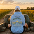 A person sitting in the bed of an old pickup truck facing a field of sunflowers at sunset, wearing a light blue hoodie with a large graphic on the back that reads “WANDER WHERE” and “The Sunshine Coast.”.