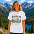 Woman wearing Wander Far Take the Scenic Route mountain hiking graphic t-shirt featuring vintage mountain landscape artwork with pine trees and sunset background.