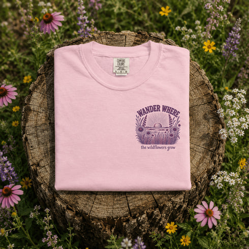 Pink sweatshirt with a purple graphic and text on a wooden stump surrounded by wildflowers