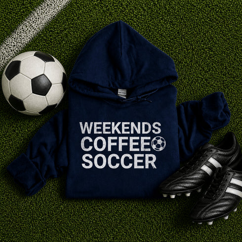 Navy hoodie with 'Weekends Coffee Soccer' text on grass with soccer ball and shoes