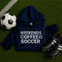 Navy hoodie with 'Weekends Coffee Soccer' text on grass with soccer ball and shoes