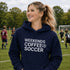 Woman wearing a navy hoodie with 'Weekends Coffee Soccer' text on a soccer field.