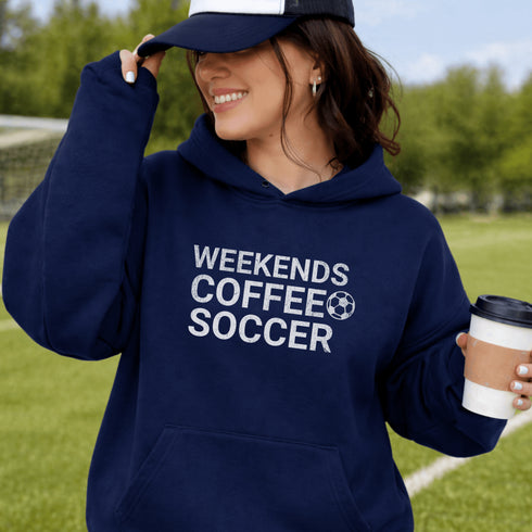 Person wearing a navy hoodie with 'Weekends Coffee Soccer' text, holding a coffee cup outdoors.