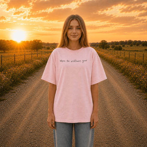 Woman wearing a white Comfort Colors 1717 t-shirt featuring a Prairie Roads Where the Wildflowers Grow prairie sunset wildflower back graphic on a gravel road at sunset.