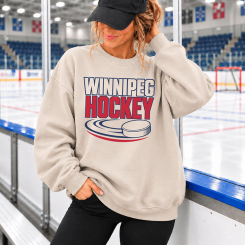 Winnipeg Hockey unisex crewneck sweatshirt featuring vintage navy and red collegiate lettering with a hockey puck graphic, designed by Prairie Life Co.