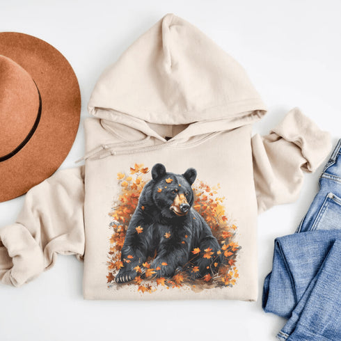 Featuring a detailed graphic of a black bear nestled comfortably among a colorful bed of autumn leaves, this hoodie brings warmth and woodland charm to your wardrobe.
