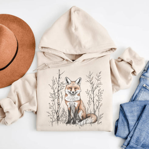 This hoodie features a stunning graphic of a vibrant red fox poised amidst the shadows and light of a lush woodland scene.