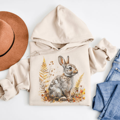 This cozy hoodie features a playful rabbit nestled among vibrant fall foliage, surrounded by the warm oranges, reds, and yellows of the season.