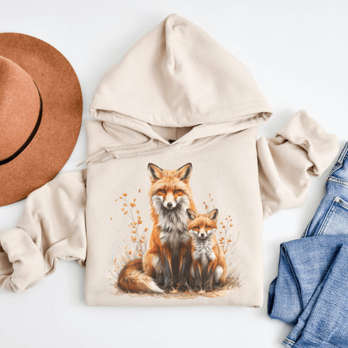 This beautifully crafted hoodie showcases a loving mother fox and her playful kit sitting in a cozy bed of fall foliage, surrounded by vibrant autumn leaves.