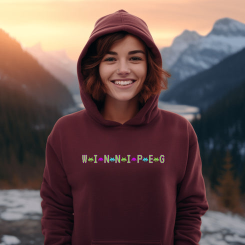 This picture showcases the Winnipeg Retro Gaming Hoodie that has a bold green gaming font with space creatures separating the Winnipeg Letters