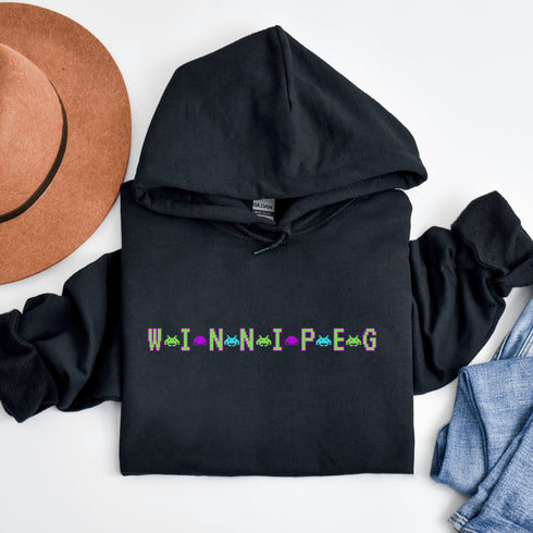 This picture showcases the Winnipeg Retro Gaming Hoodie that has a bold green gaming font with space creatures separating the Winnipeg Letters