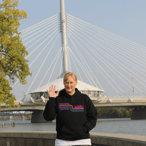 This gender neutral hoodie features A Winnipeg City Skyline and colored retro Stripes across the front.