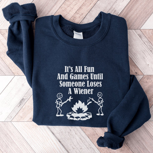 Our Camping sweatshirt features two stick people roasting wieners over a campfire with the hilarious saying, "It's All Fun & Games Until Someone Loses A Wiener."